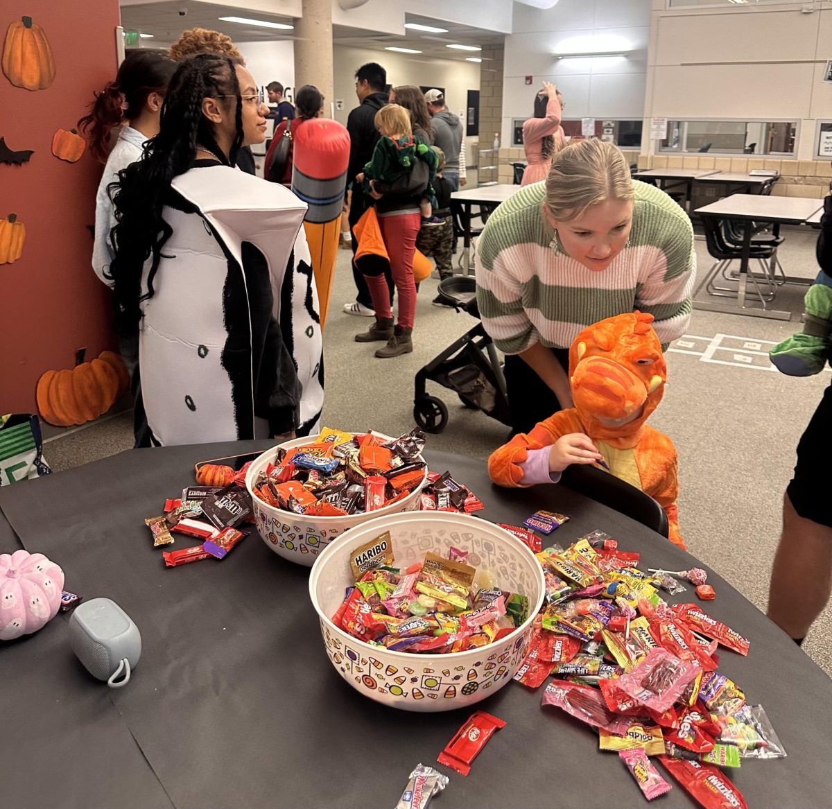 A kid dressed as a dinosaur surveys the table for the best candy.