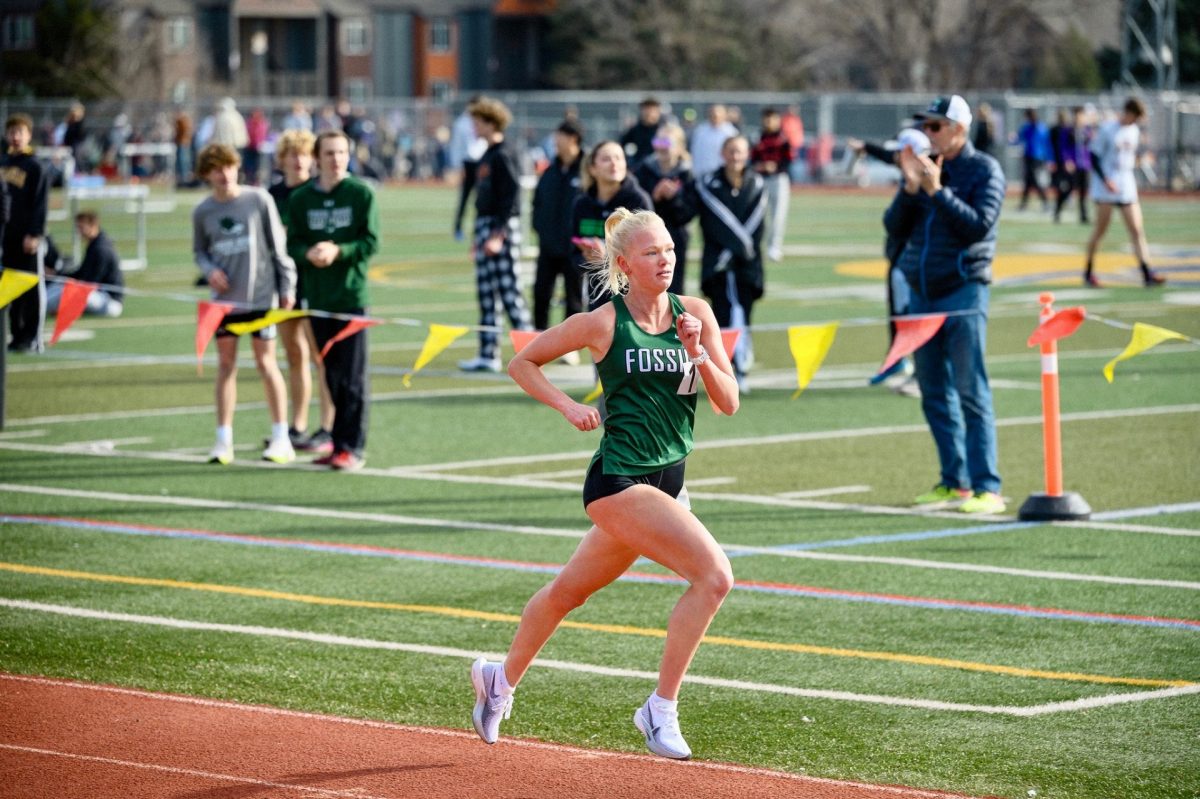 Being cheered on by teammates, Tatum Berg strides to the finish line at the Runners Roost track meet.
